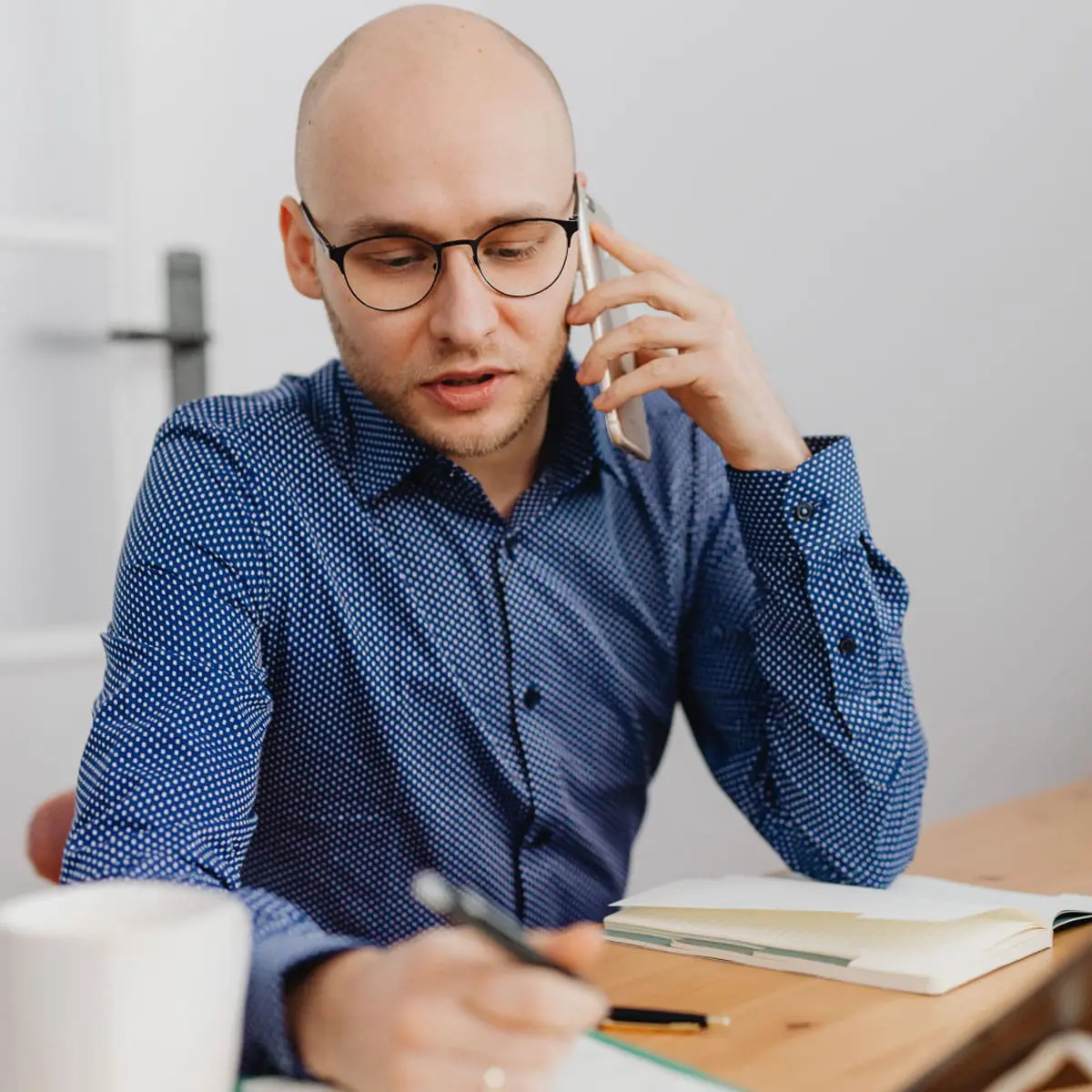 A man with a shaved head is talking on the phone and taking notes