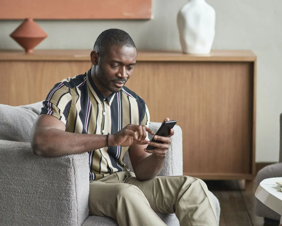A man is sitting in his living room and using his phone for the Georgia Heritage Federal Credit Union mobile banking app