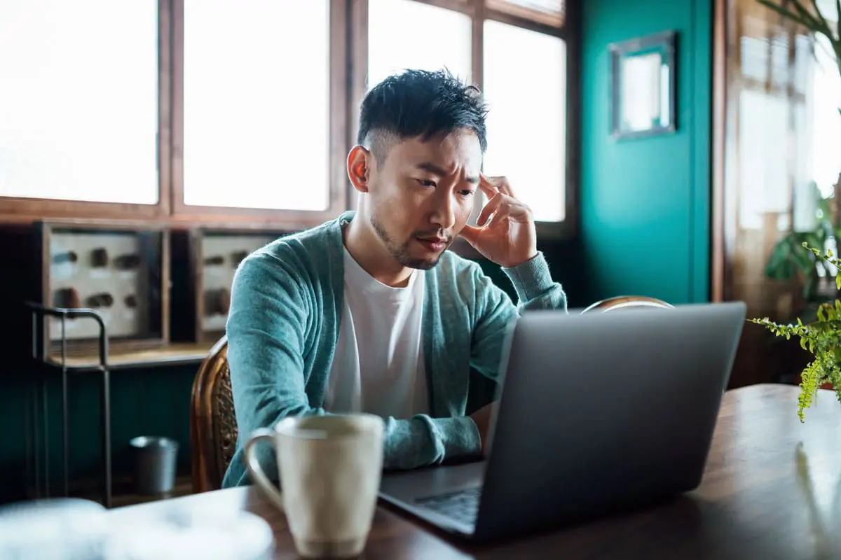A young man with a concerned look on his face is using his laptop