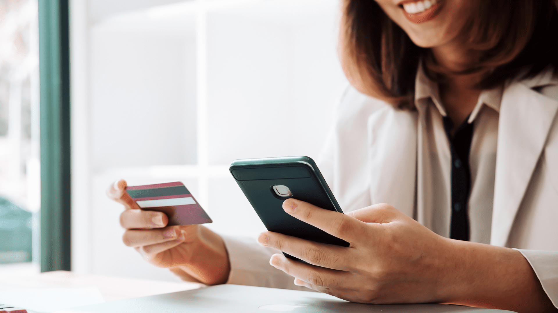 Photograph of a person holding a credit card in one hand and a smartphone in the other, using a GHFCU credit card as a smarter way to shop
