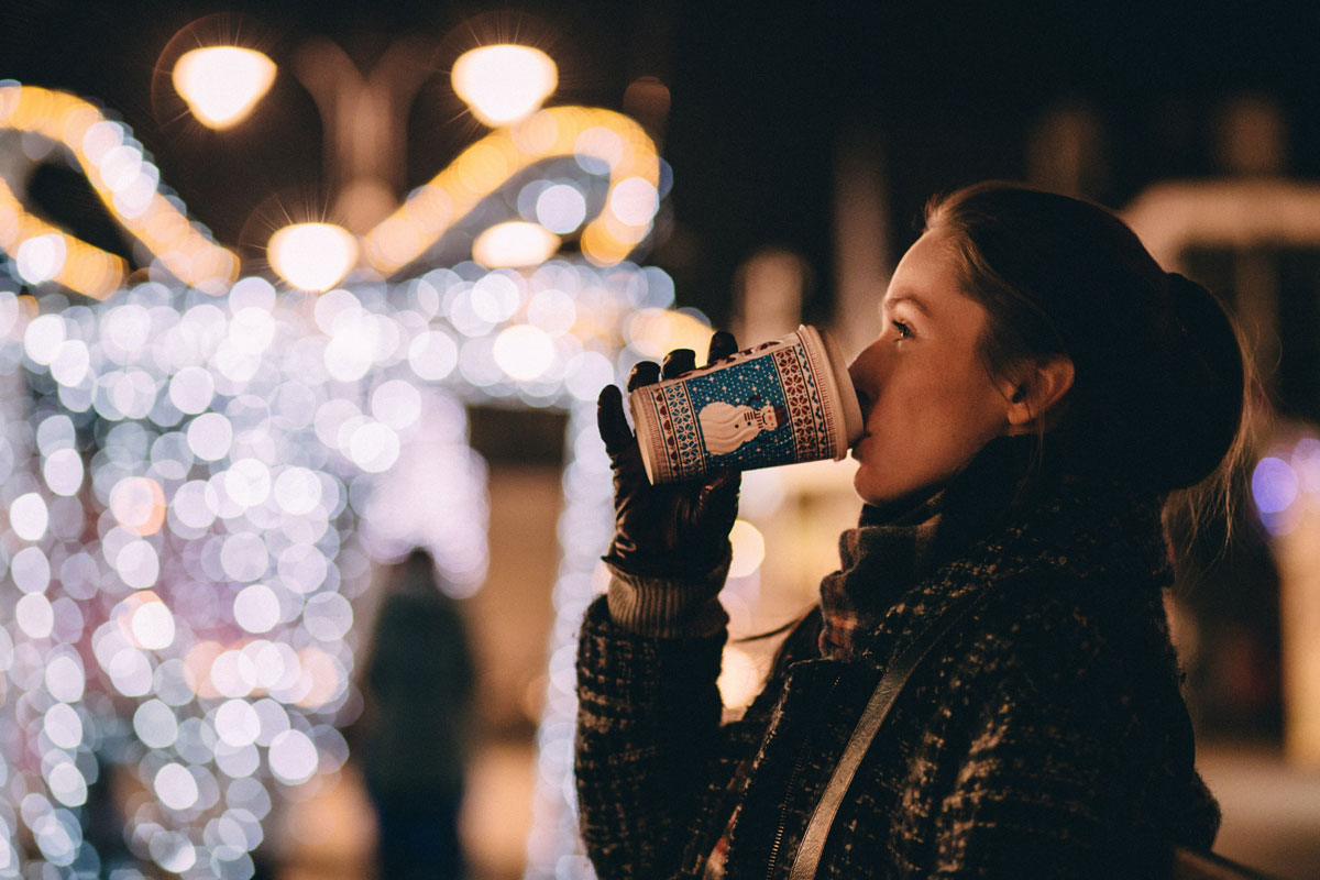 A woman is sipping coffee at night during a Christmas event