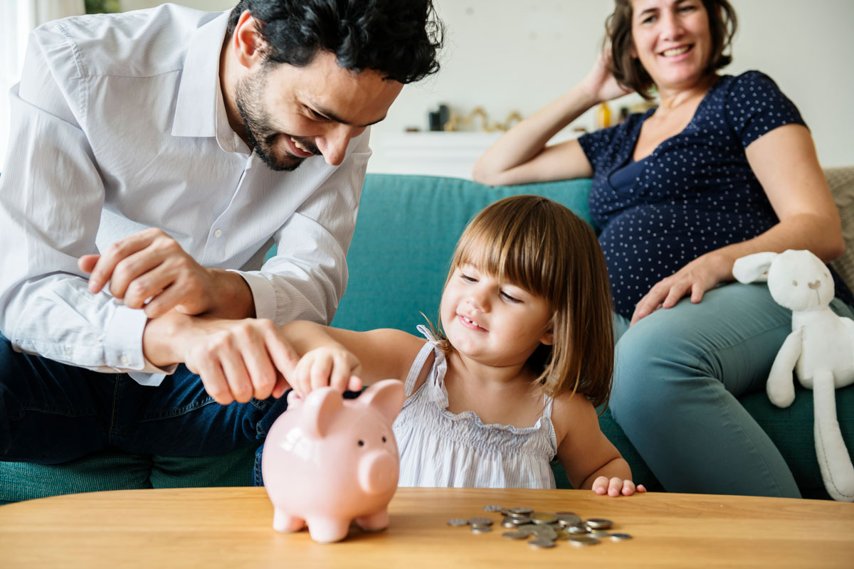 A young couple is teaching their child how to save money using a piggy bank