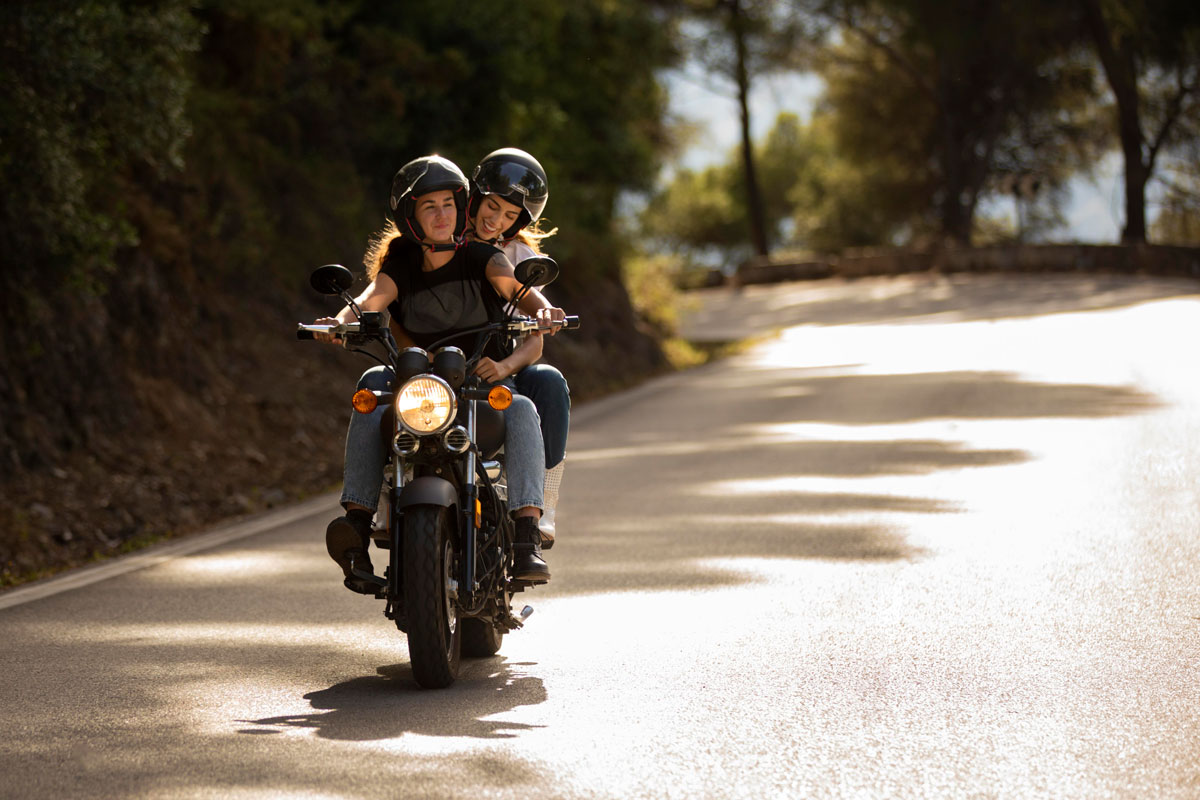 Two friends are riding a motorcycle on an empty road