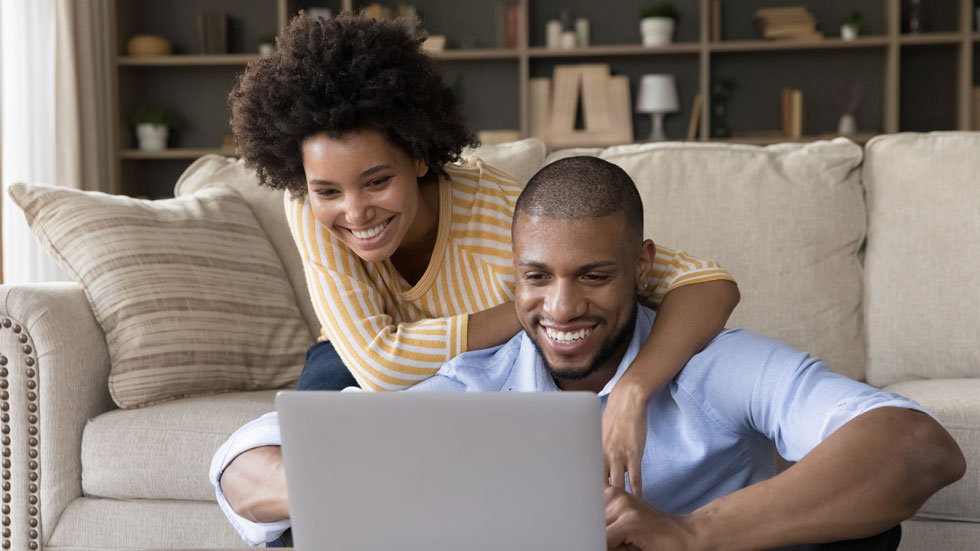 A young couple is sitting in front of a laptop together with smiles on both of their faces