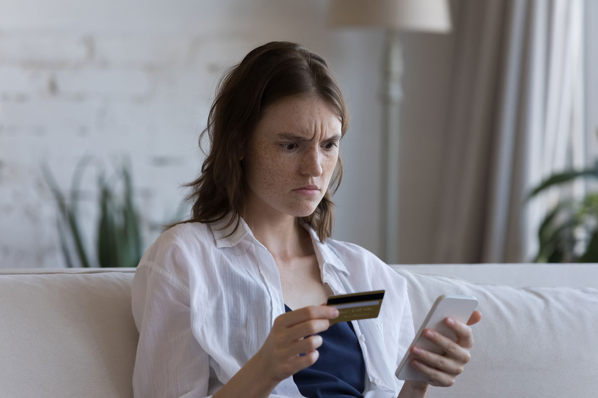 A woman with a concerned look on her face is holding her phone and debit card
