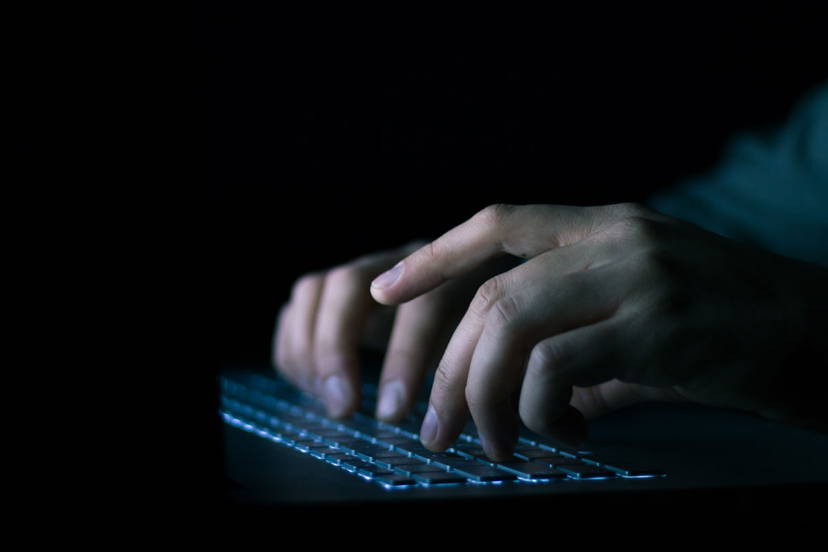 A man in a dark room is typing on a keyboard